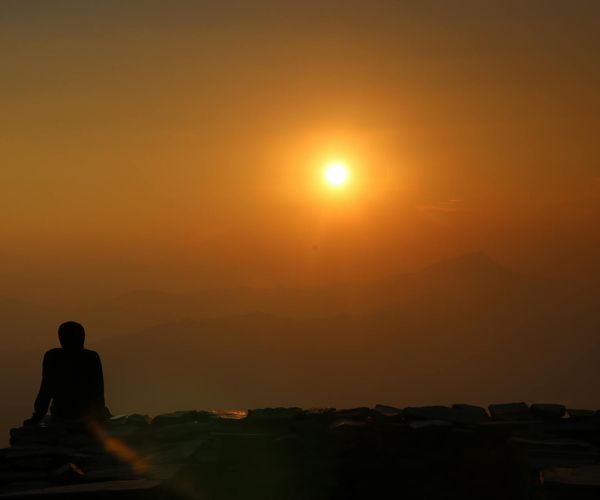 Silhouette of a person meditating against a warm background.